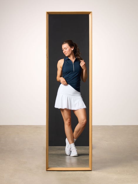 Woman reflected in mirrior wearing a navy polo tank and white tennis skirt.