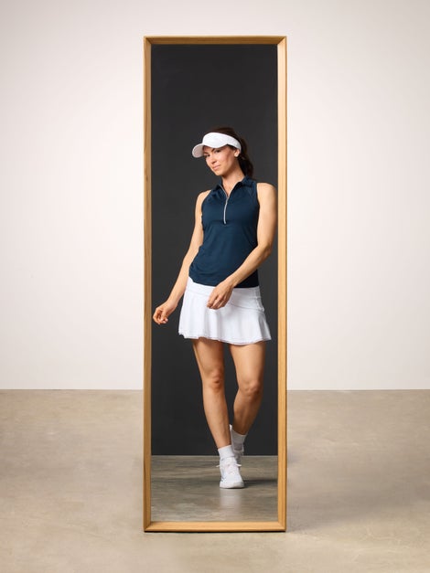 Woman reflected in mirrior wearing a navy polo tank and white tennis skirt.