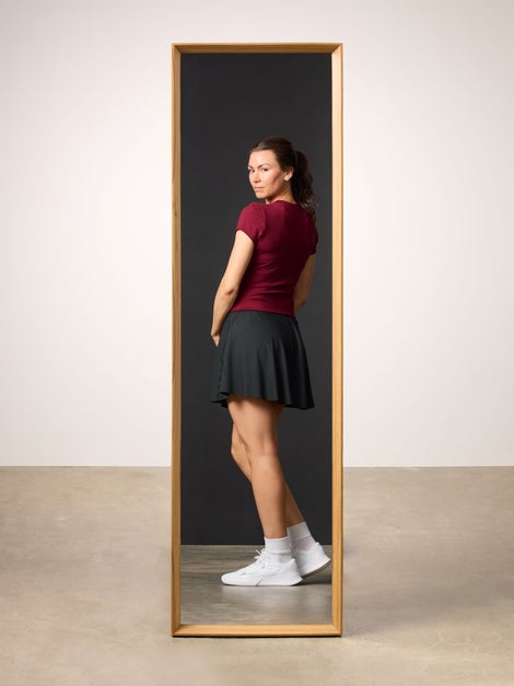 Woman reflected in mirror wearing a burgundy top and black tennis skirt. 