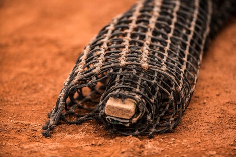 Tennis net rolled up on top of clay. 