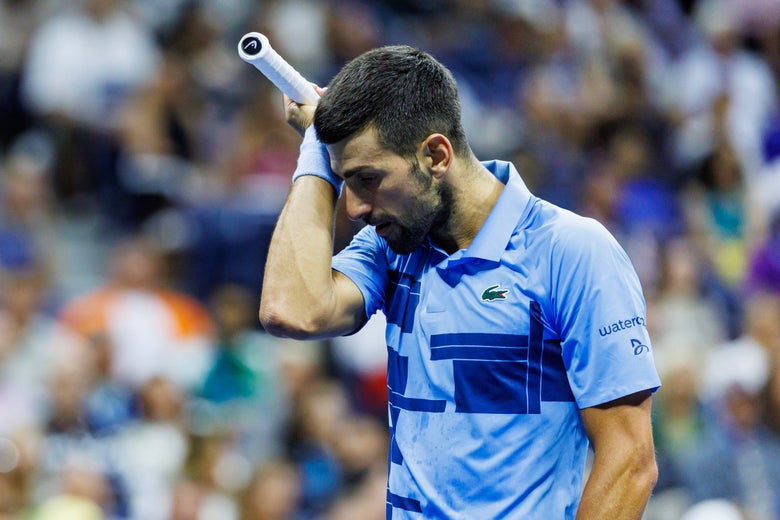 Novak Djokovic wipes his brow while wearing his blue Lacoste polo.