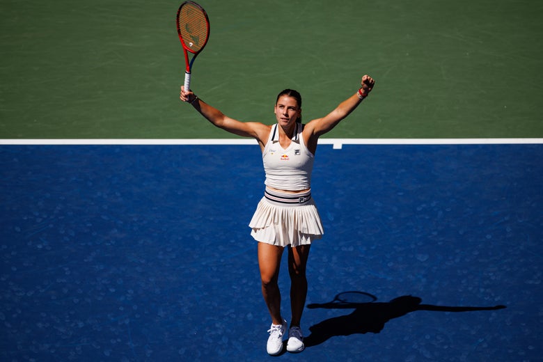 Emma Navarro raises her arms in celebration wearing an off white tank top and tennis skirt