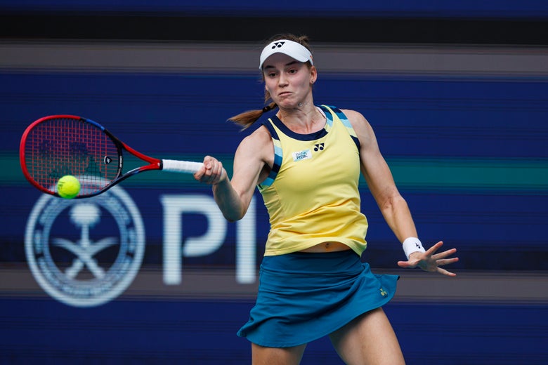 Elena Rybakina hits a forehand while wearing a yellow tank top and blue skirt.