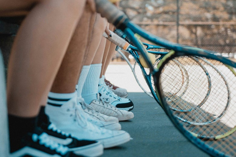 Tennis players sitting on a bench lined up for summer camp. 