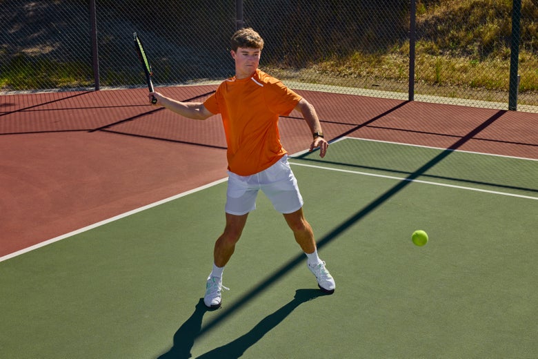 Player wearing an orange shirt and white shorts hitting a jumping forehand.