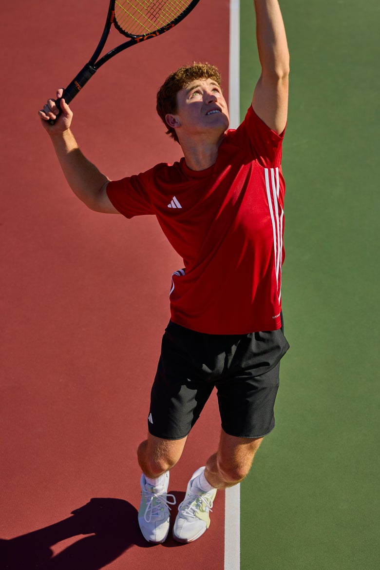 Player serving a ball wearing the adidas Tabela Top in red